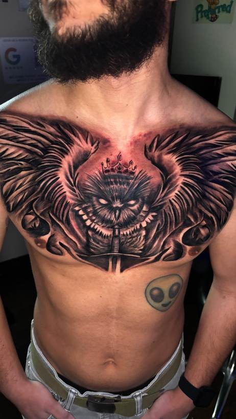 Black and grey crowned owl chest piece with wings and a sword. Tattoo by a Thorn and Oath artist.