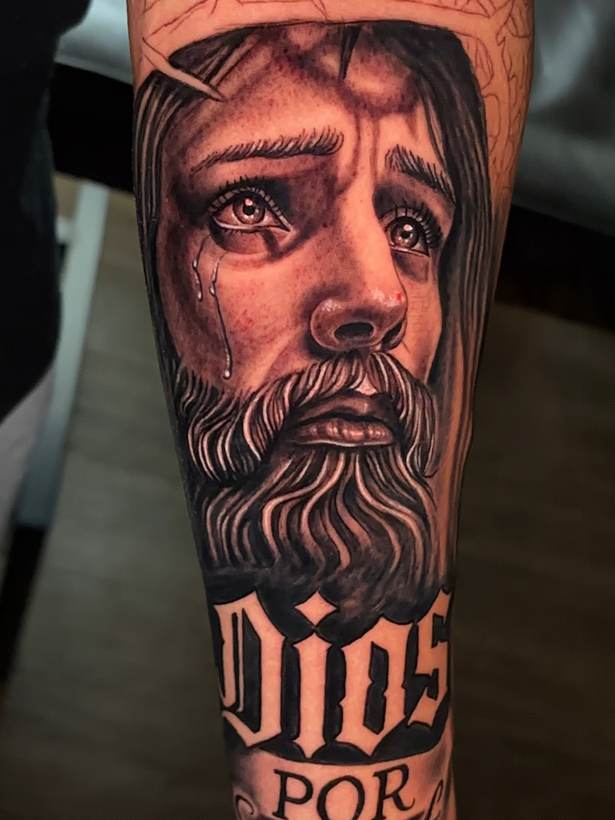 Black and grey portrait forearm piece with lettering. Tattoo by a Thorn and Oath artist.