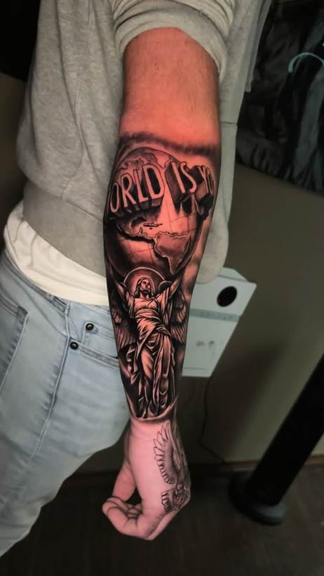 Black and grey forearm piece with a globe and statue. Tattoo by a Thorn and Oath artist.