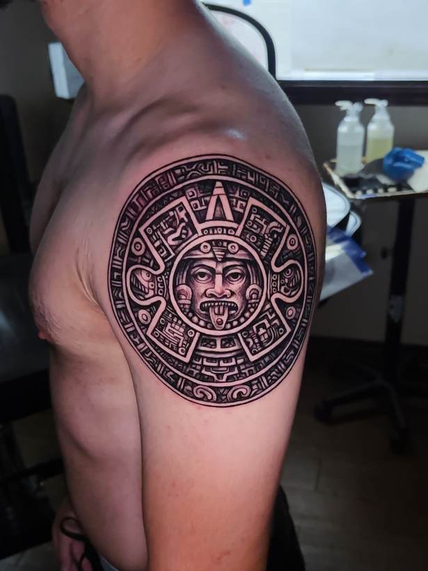 Black and grey stone calendar shoulder piece. Tattoo by a Thorn and Oath artist.